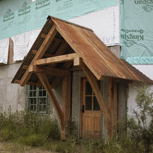 Full view of a timber framed porch structure with a rusty corrugated metal roof over a wooden entry door