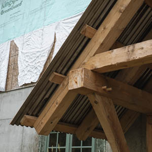 Close-up of traditional timber frame joinery featuring wooden pegs and heavy beams under a metal roof