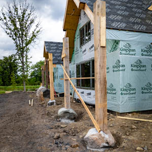 Perspective view of a White Oak porch roof under construction with timber posts anchored to natural rock footings.